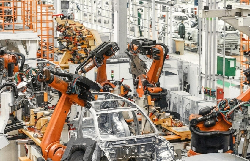 A watercolor image of a factory where orange robots are assembling a white vehicle.